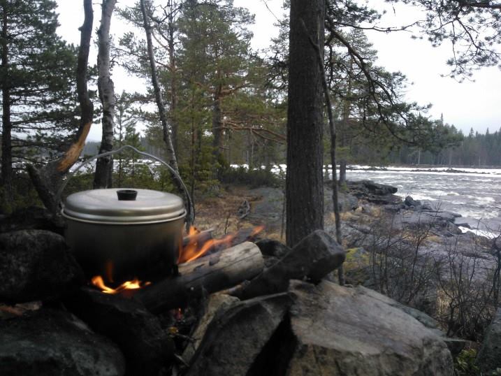 Cooking pot on a campfire with river and forest in background.
