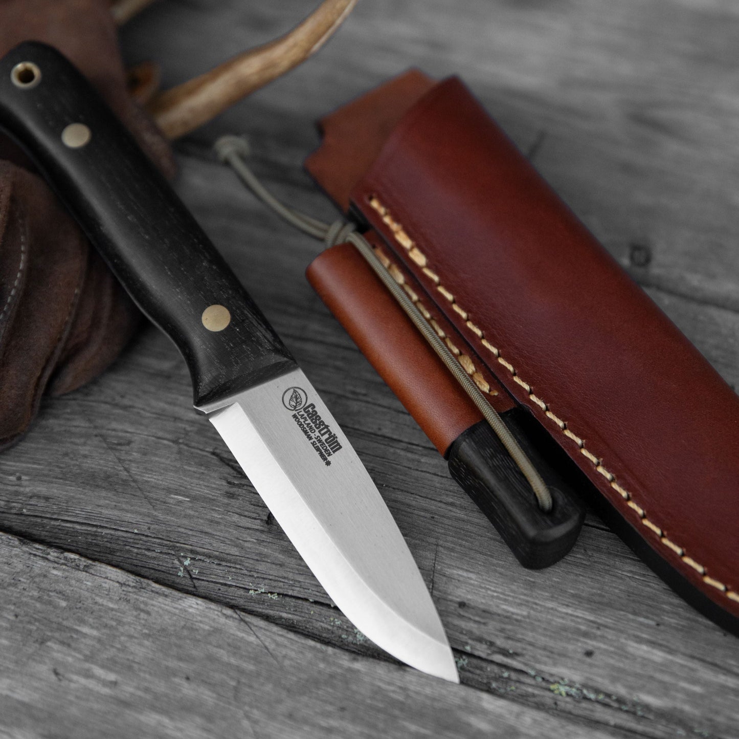 Casström Woodsman knife in bog oak, resting on a glove and showing the leather sheath and integral firesteel loop. with matching bog oak firesteel.