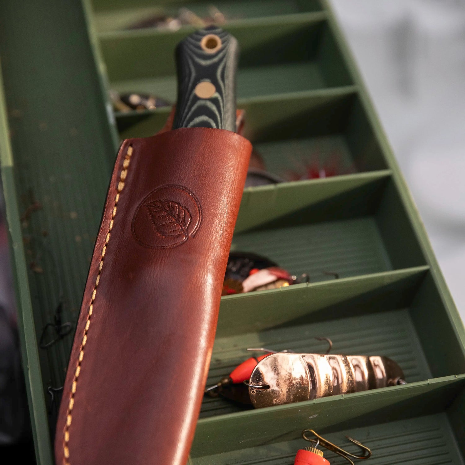 No.8 SFK Scandi Grind, green micarta handle, embossed leather sheath, sitting atop a fishing tackle box.