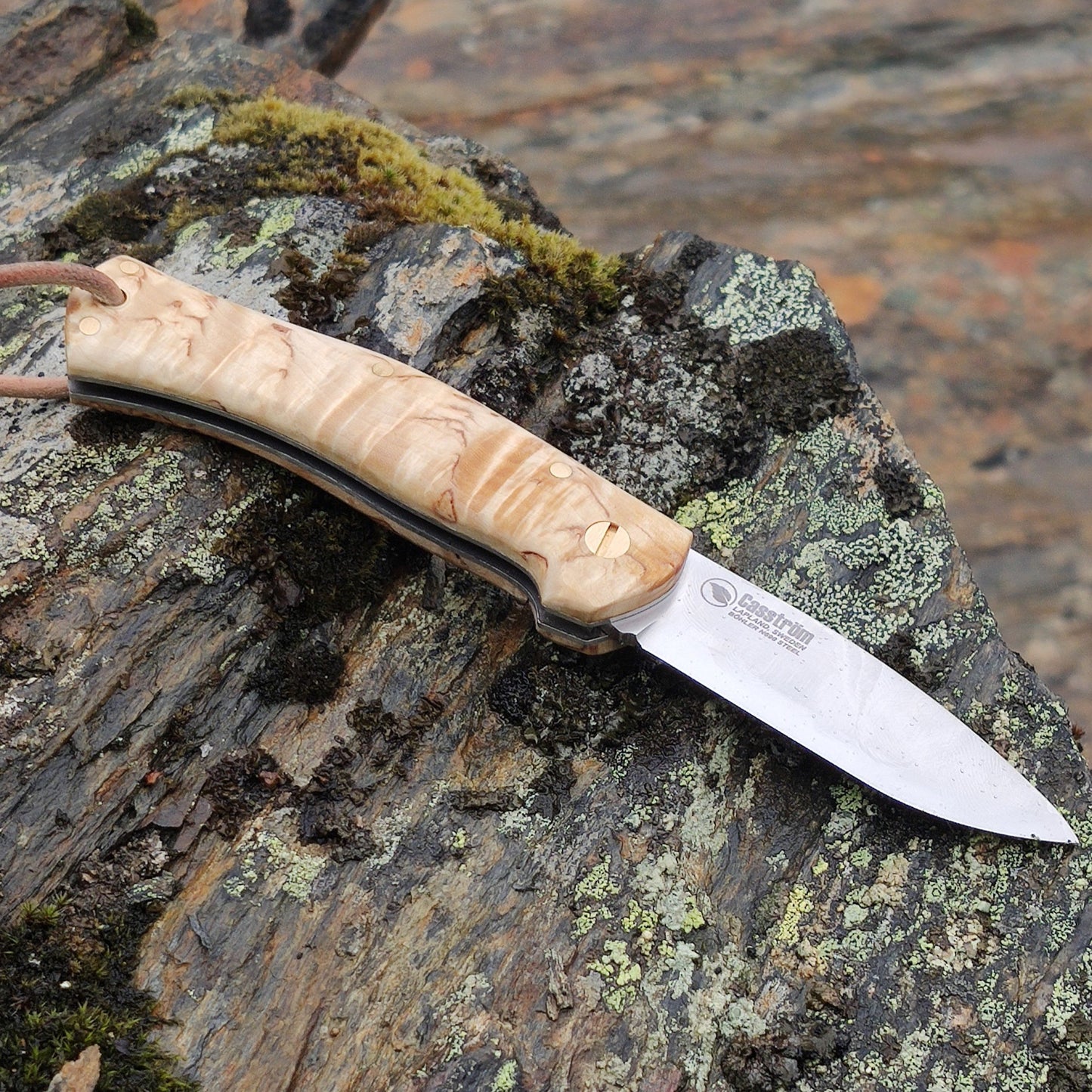 Casström Lars Fält Slip Joint - UK leagal EDC knife, with curly birch handle, lying on a rock.