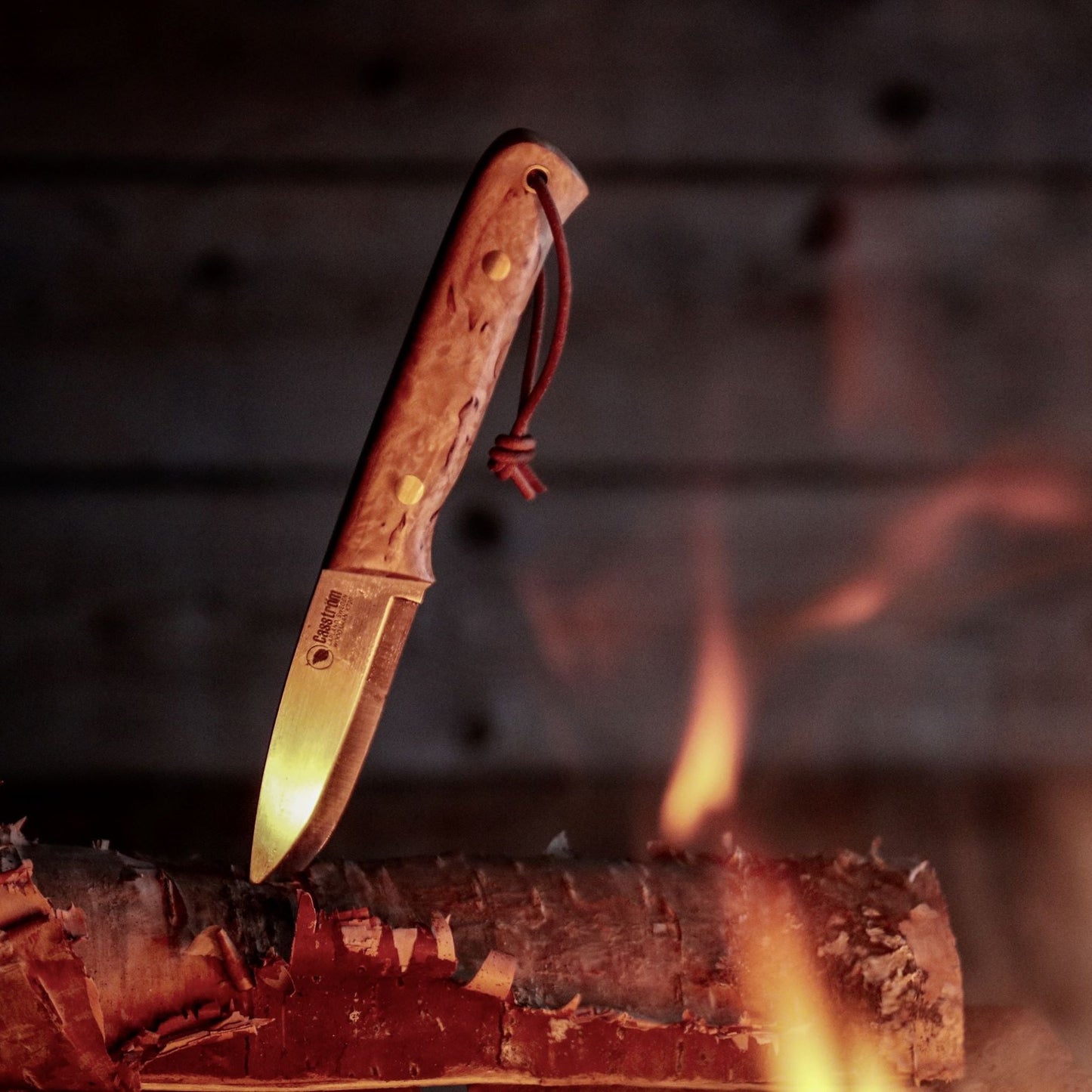 The Casstrom Woodsman knife next to a campfire, showing the curly birch handle and scandi grind blade