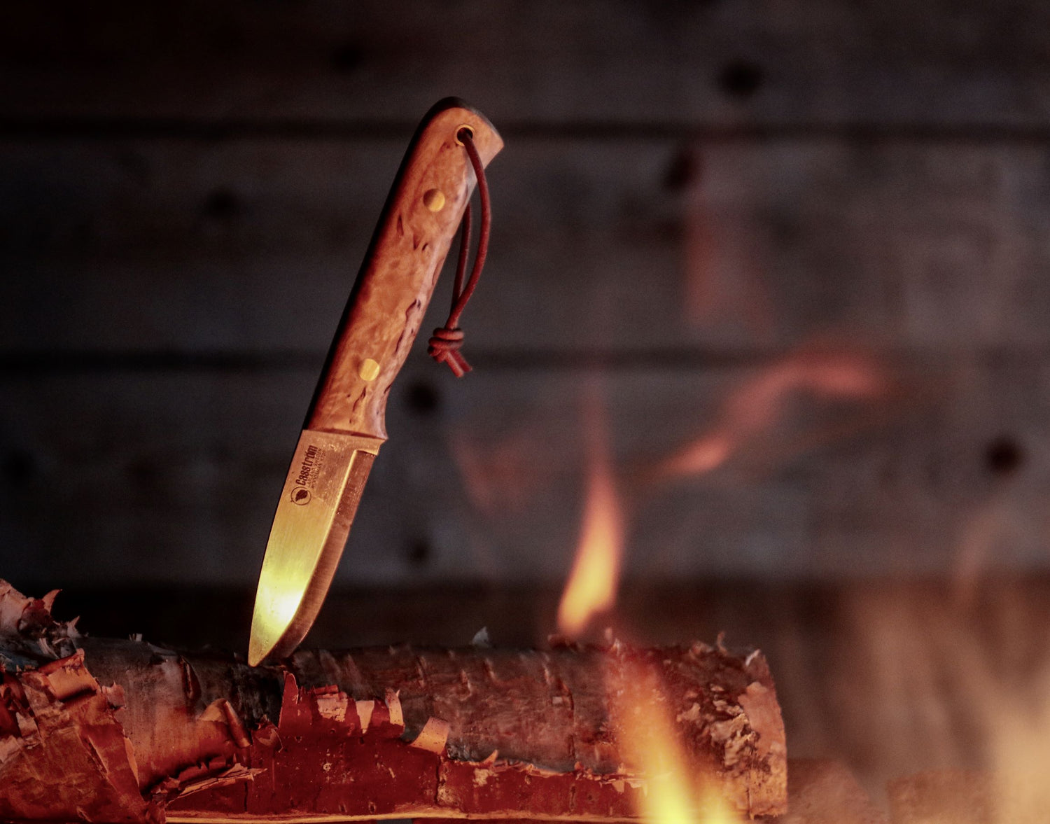 The Casstrom Woodsman knife next to a campfire, showing the curly birch handle and scandi grind blade