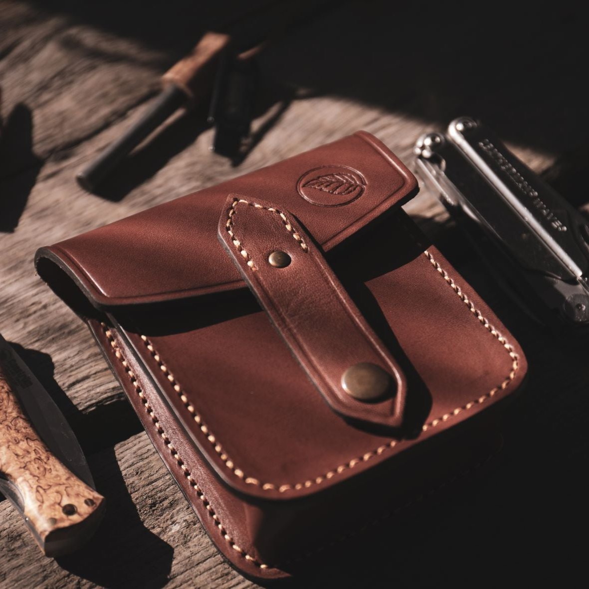 Casström Possibles Pouch and an assortment of rifle cartridges and folding knives on a wooden table