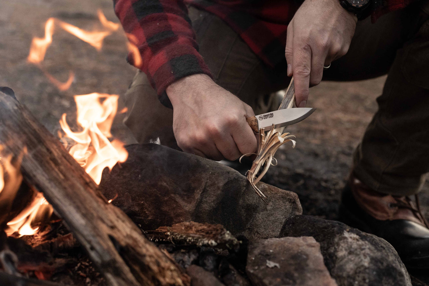 Person lighting a fire with a Casström No.8 SFK knife near a campfire