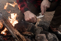 Person lighting a fire with a Casström No.8 SFK knife near a campfire