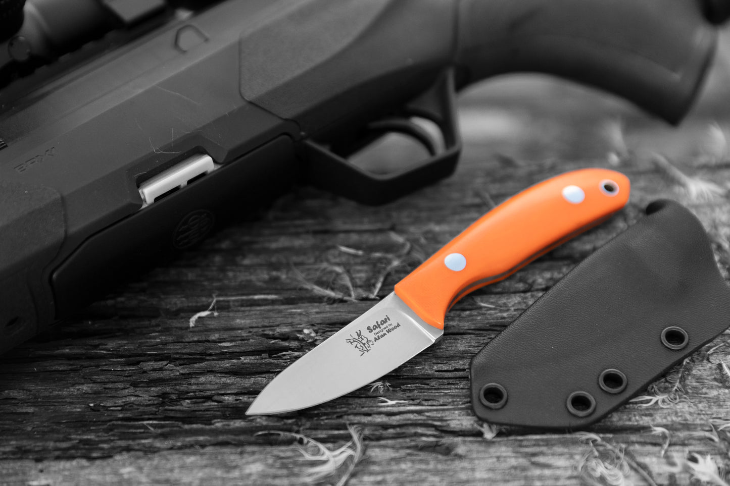 Close up of a Casström Safari Mini-Hunter knife with Kydex sheath, lying next to a hunting rifle