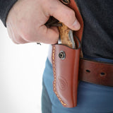 Man drawing a Casström folding knife from a premium leather belt pouch during everyday carry use outdoors.